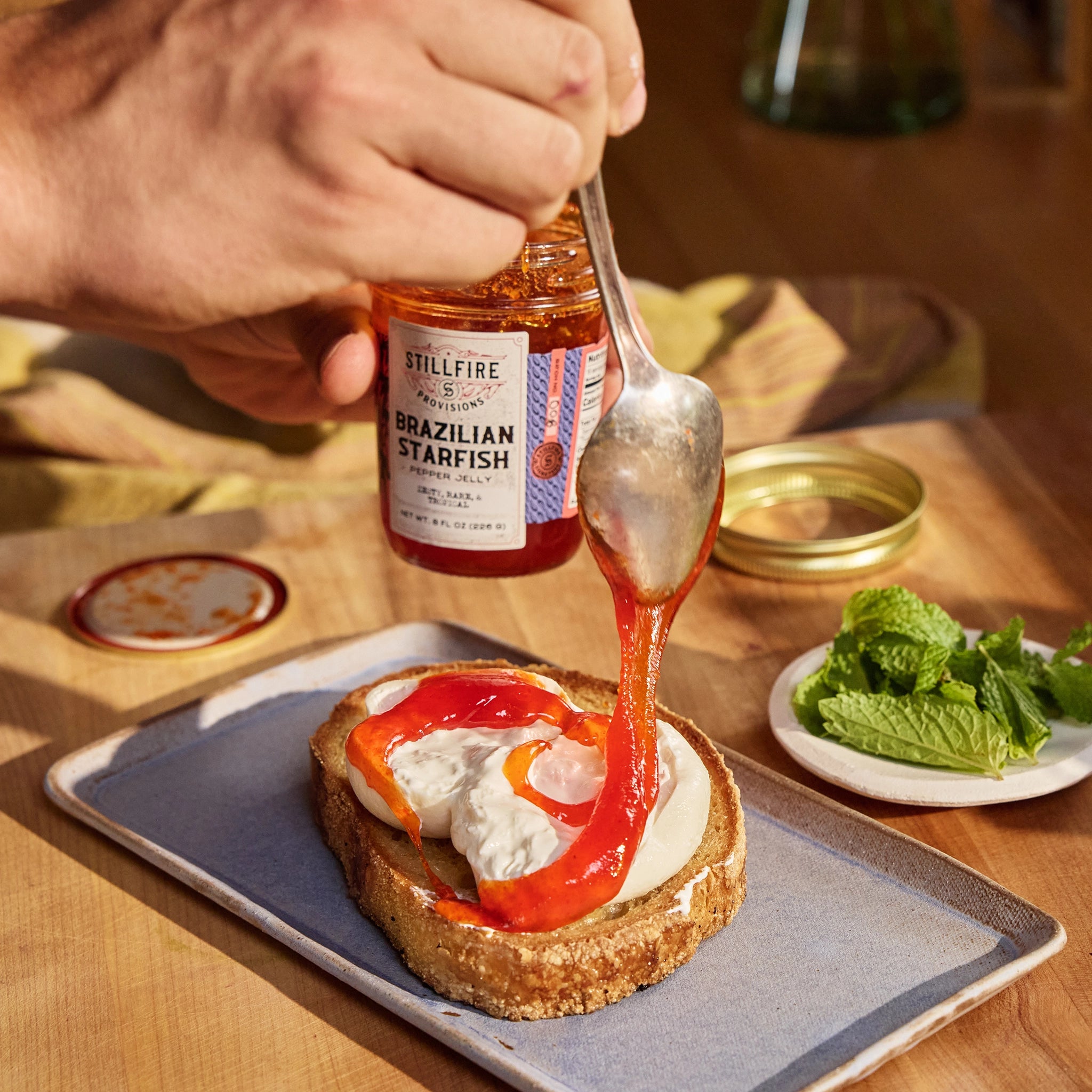 Brazilian Starfish Pepper Jelly being spooned over a burrata cheese on toast by a professional chef.