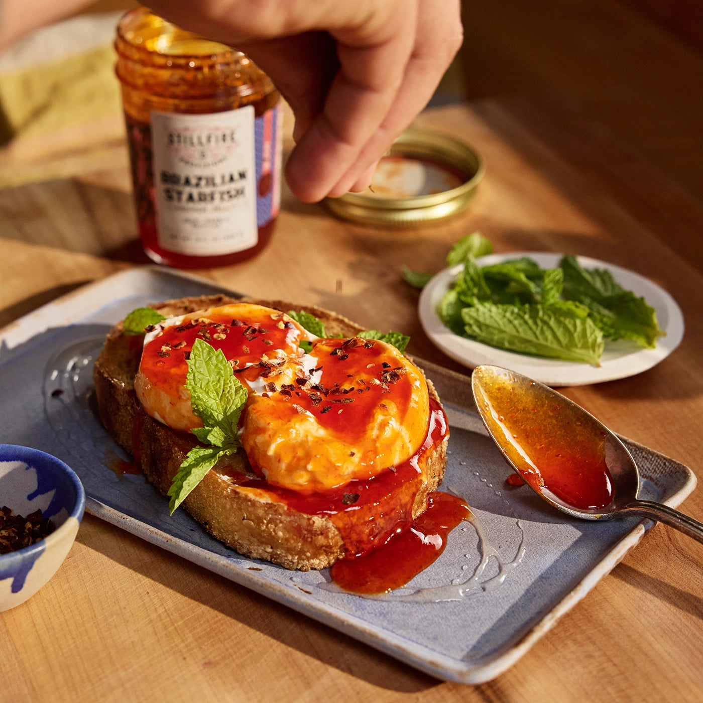 Toast with tomato and cheese, garnished with herbs, on a wooden table with a jar of jam.