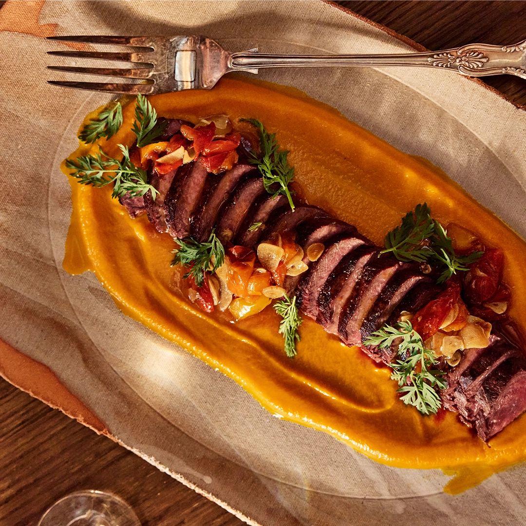 Sliced oynx tenderloin with vegetables on a decorative plate with a fork.