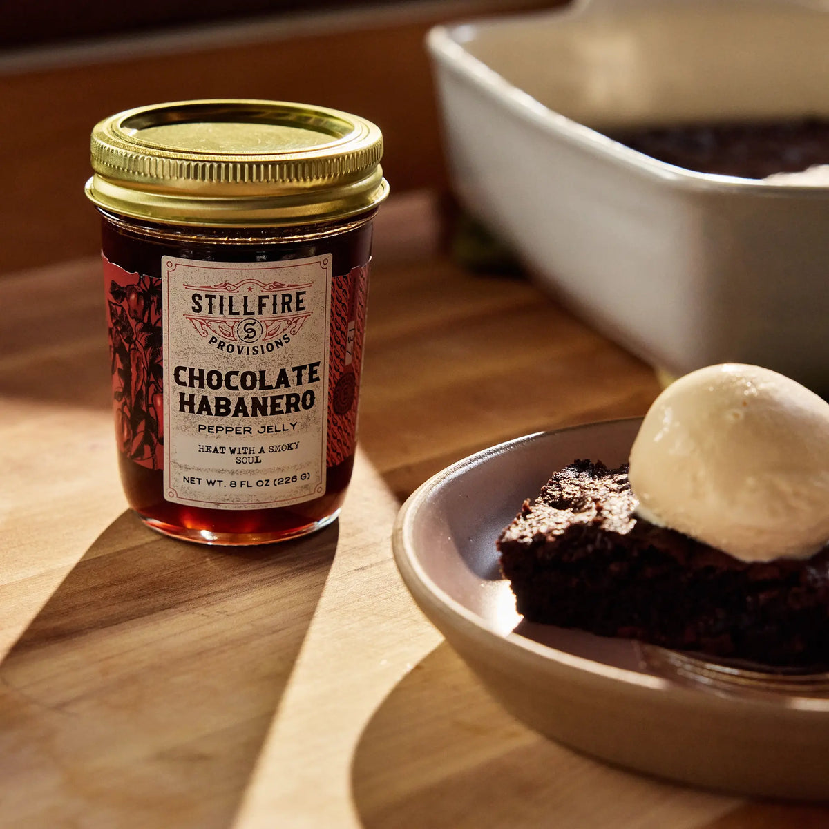 Chocolate Habanero Pepper Jelly on wood kitchen countertop next to a chocolate brownie with vanilla ice cream.
