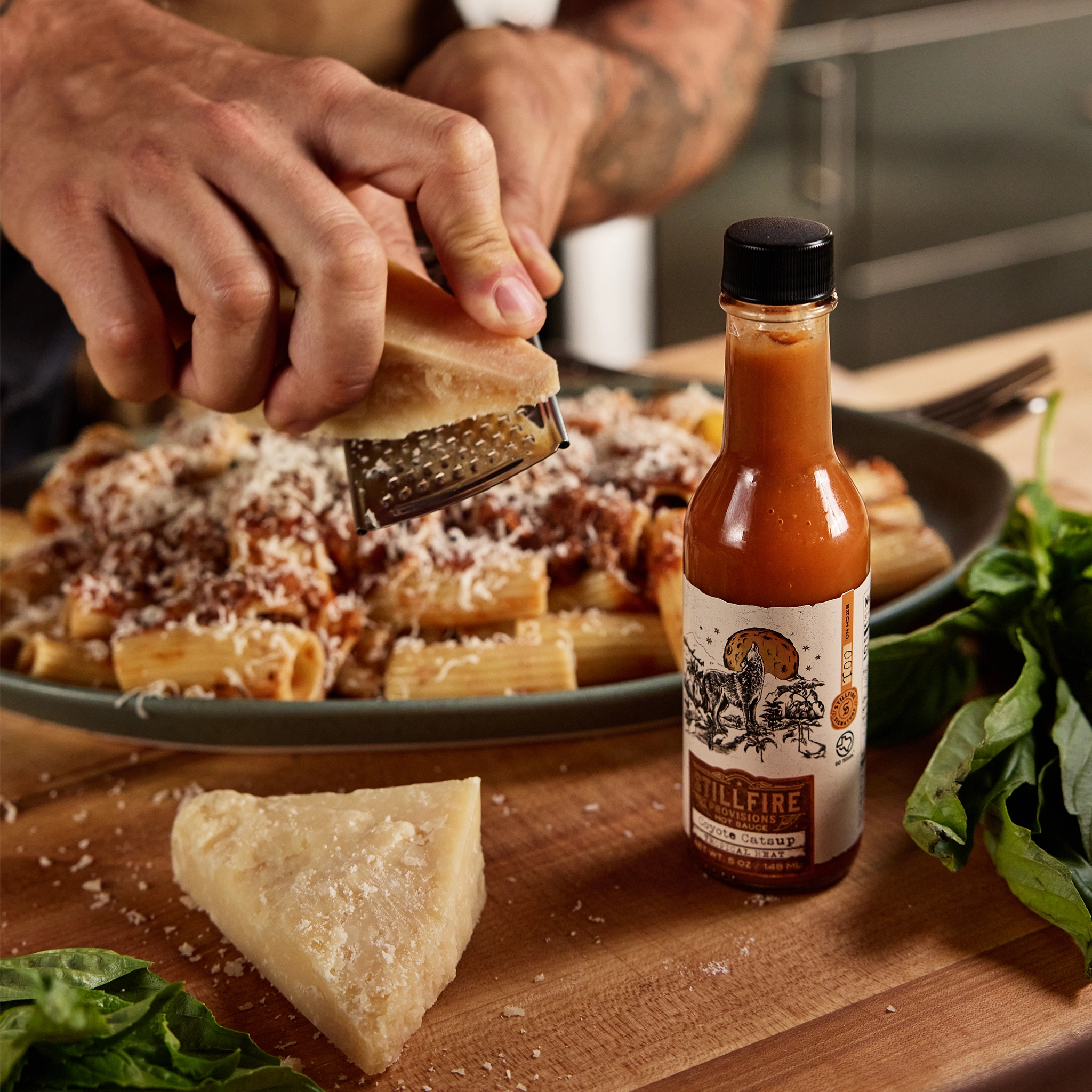 Coyote Catsup Hot Sauce next to a Bolognese dish while a chef grates cheese.
