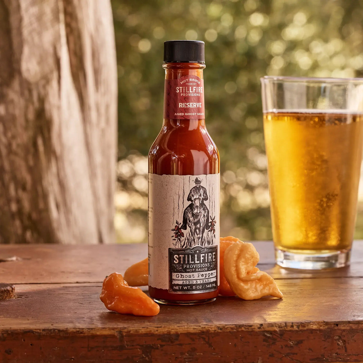 Ghost Pepper Hot Sauce next to fresh peppers on a wood table outside