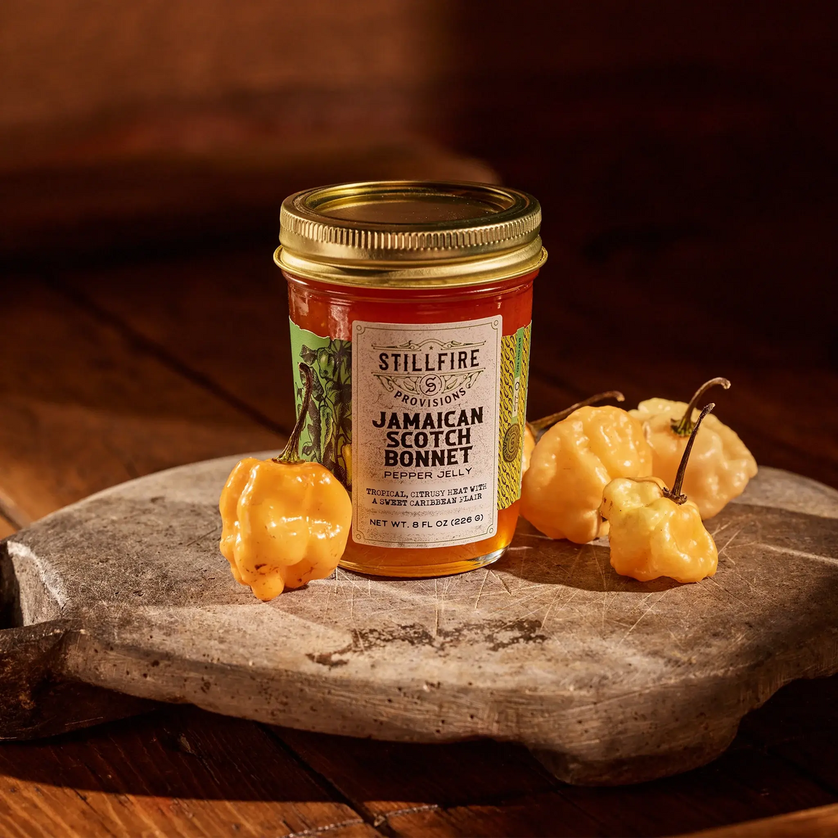 Jamaican Scotch Bonnet Pepper Jelly next to Jamaican Scotch Bonnet peppers on a wood cutting board.