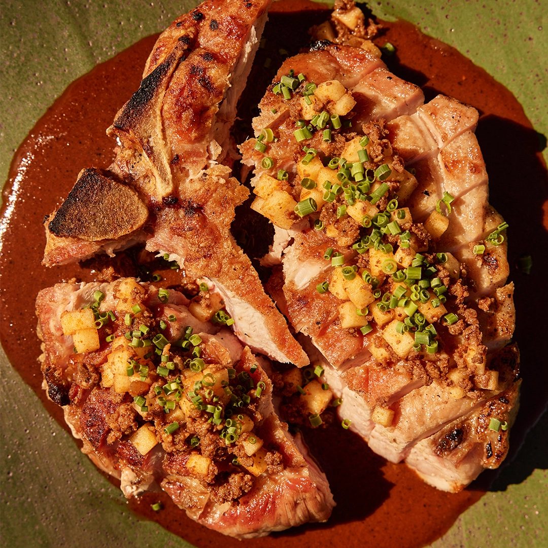 Grilled pork chops with a brown sauce and garnish on a green plate
