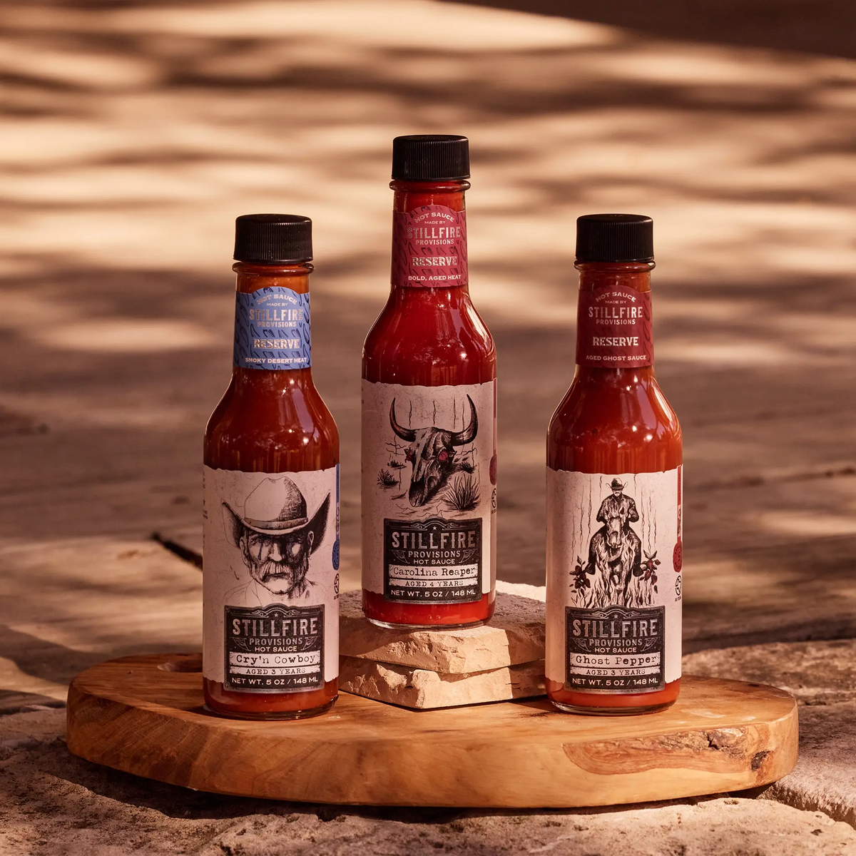 Three bottles of Stillfire Provisions hot sauce on a wooden stand with a rustic background.