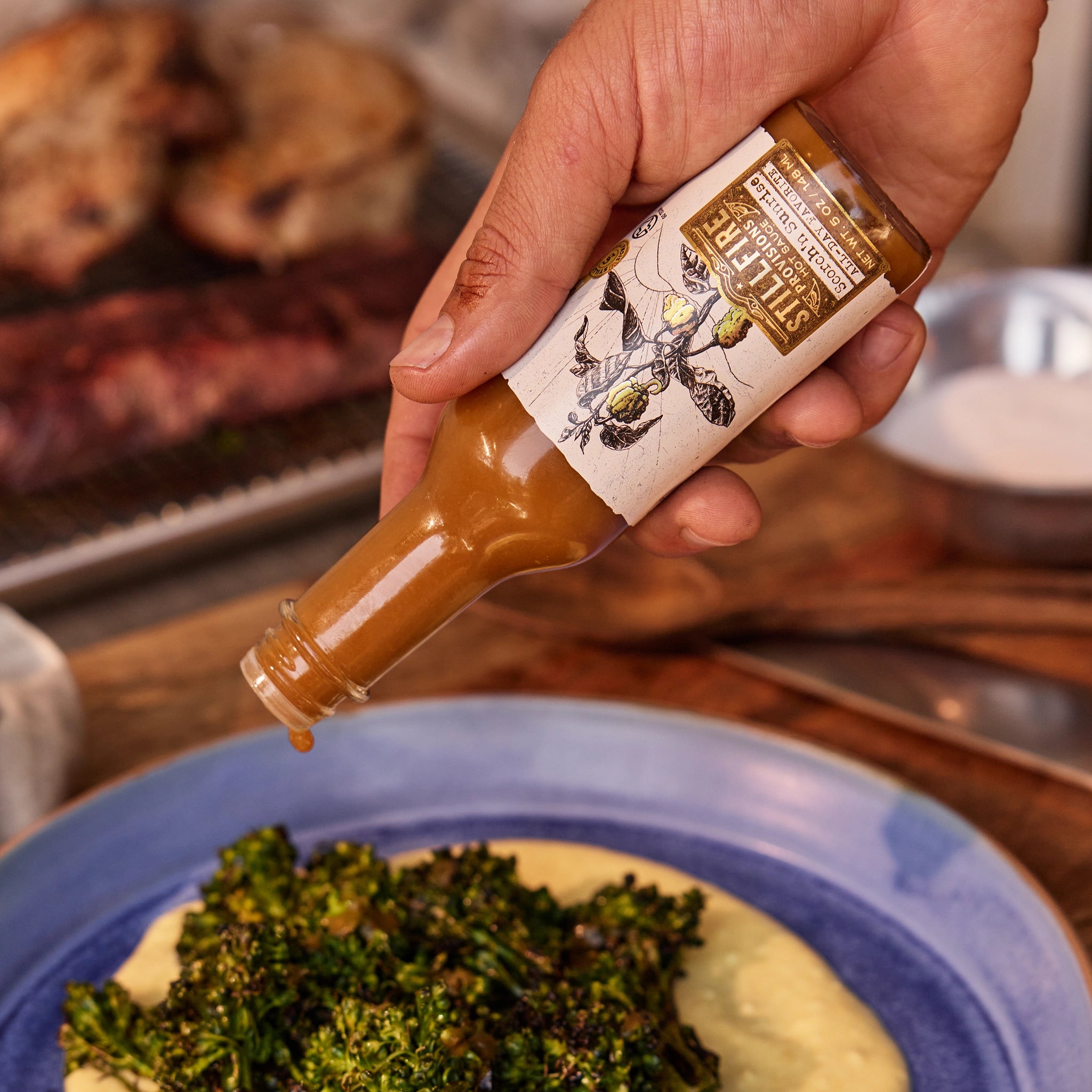 Male hand pouring Scorch'n Sunrise Hot Sauce over a gourmet blue dish.