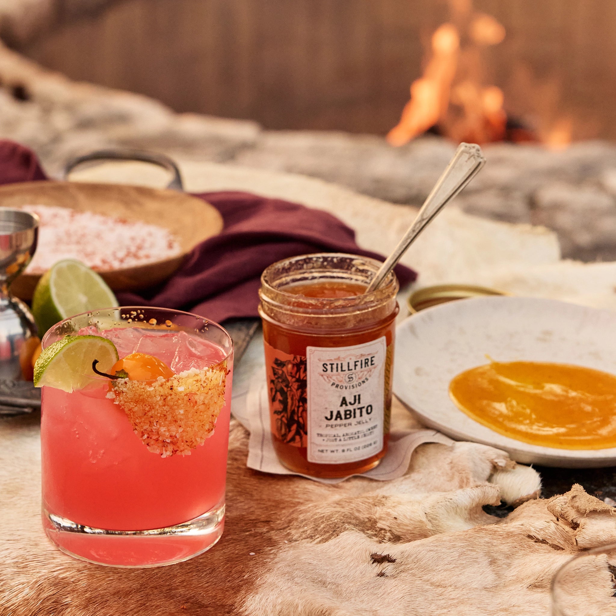 Aji Jabito Hot Sauce next to pink margarita next to a fire.