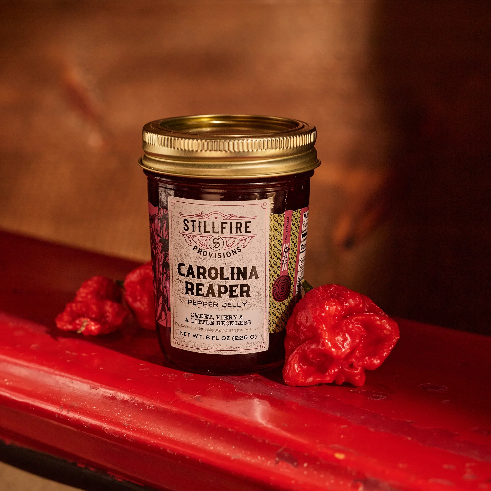 Carolina Reaper Hot Pepper Jelly next to Carolina Reaper peppers on a red metal shelf