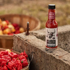 Carolina Reaper Hot Sauce next to hot peppers in baskets