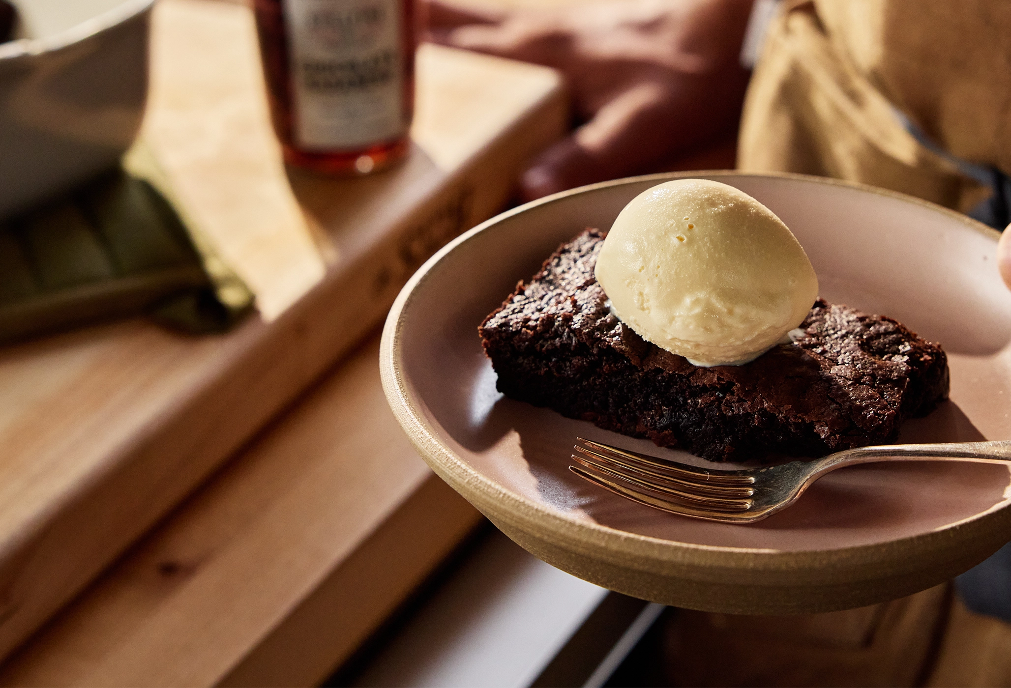 Brownies with ice cream on a plate with a fork, placed on a wooden surface.