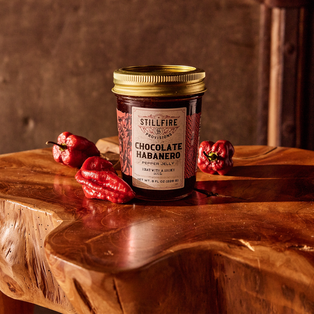 Chocolate Habanero Pepper Jelly next to Chocolate Habanero peppers on a wood table.