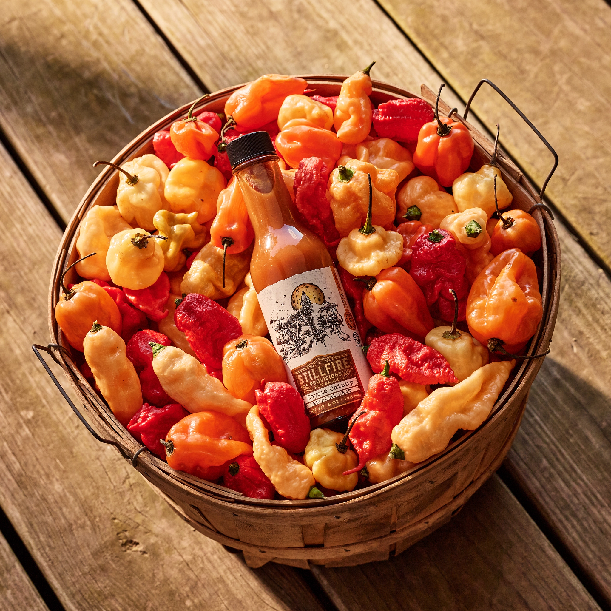 Coyote Catsup Hot Sauce in a basket of peppers on a wood porch background.
