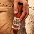 Coyote Catsup Hot Sauce being held by a male hand against a rock backdrop.