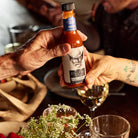 Cry'n Cowboy Hot Sauce being passed by two hands at dinner table.