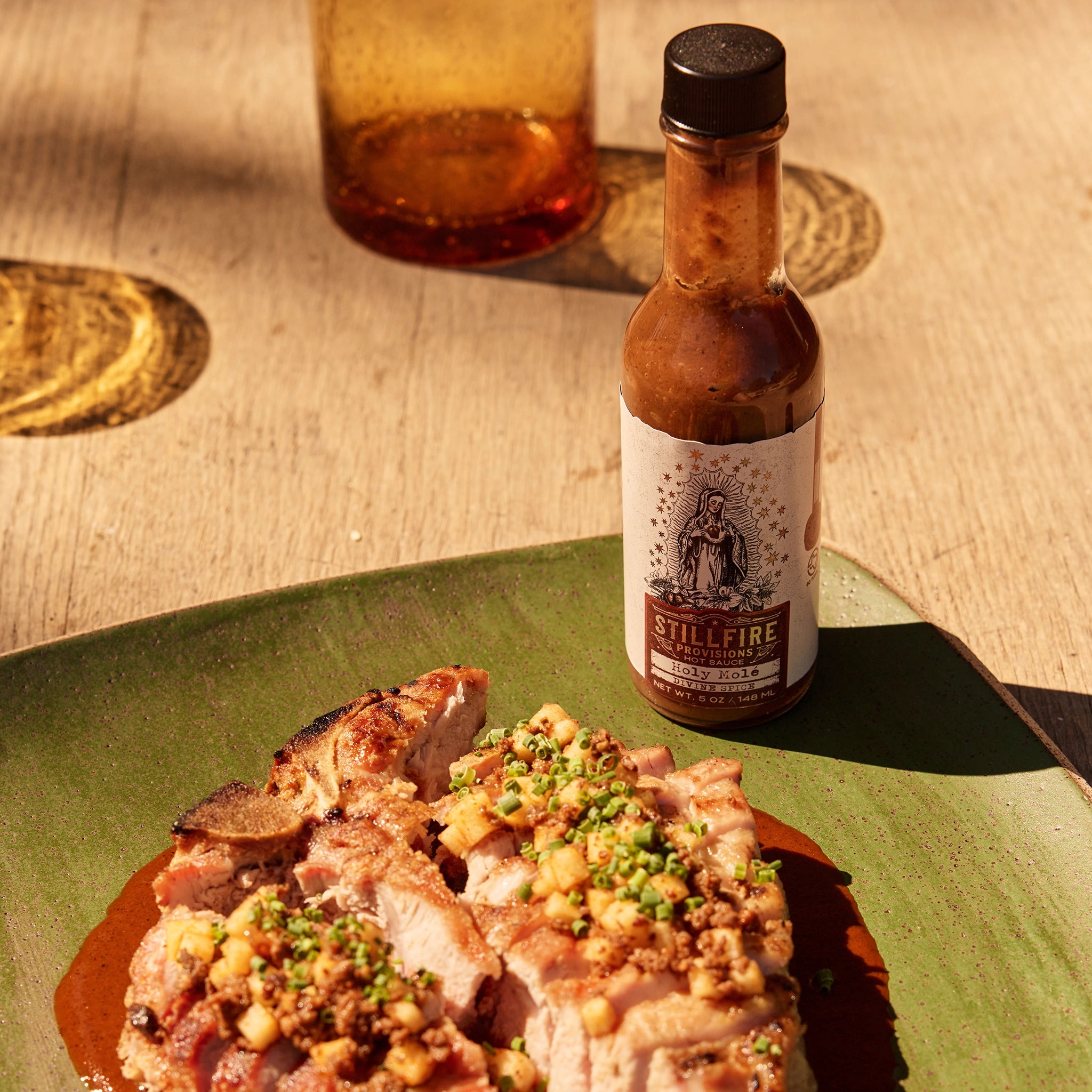 Holy Mole Hot Sauce next to gourmet pork chop dish on a wood table.