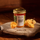Jamaican Scotch Bonnet Pepper Jelly next to Jamaican Scotch Bonnet peppers on a wood cutting board.