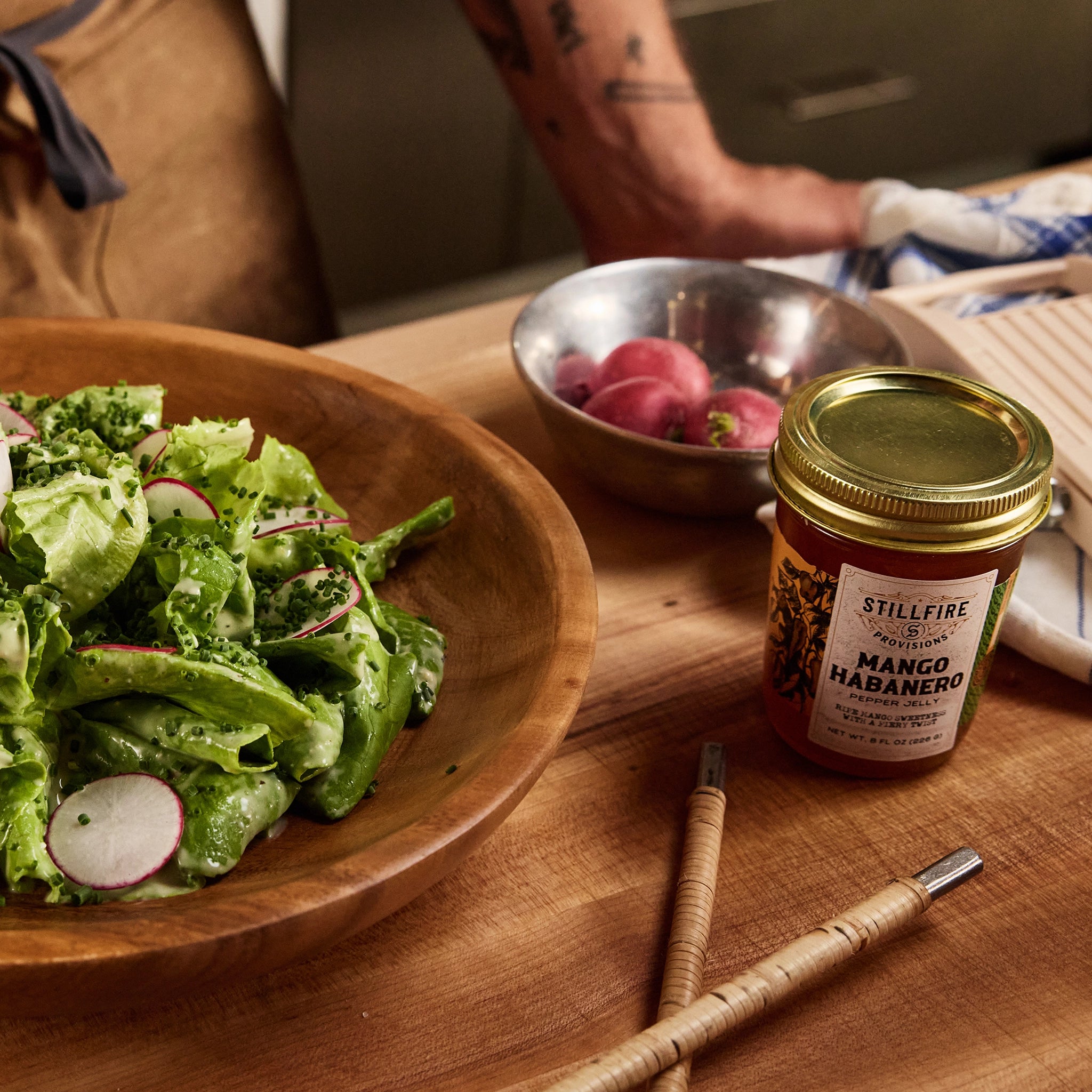 Mango Habanero Pepper Jelly next to salad on a wood table next to a chef.